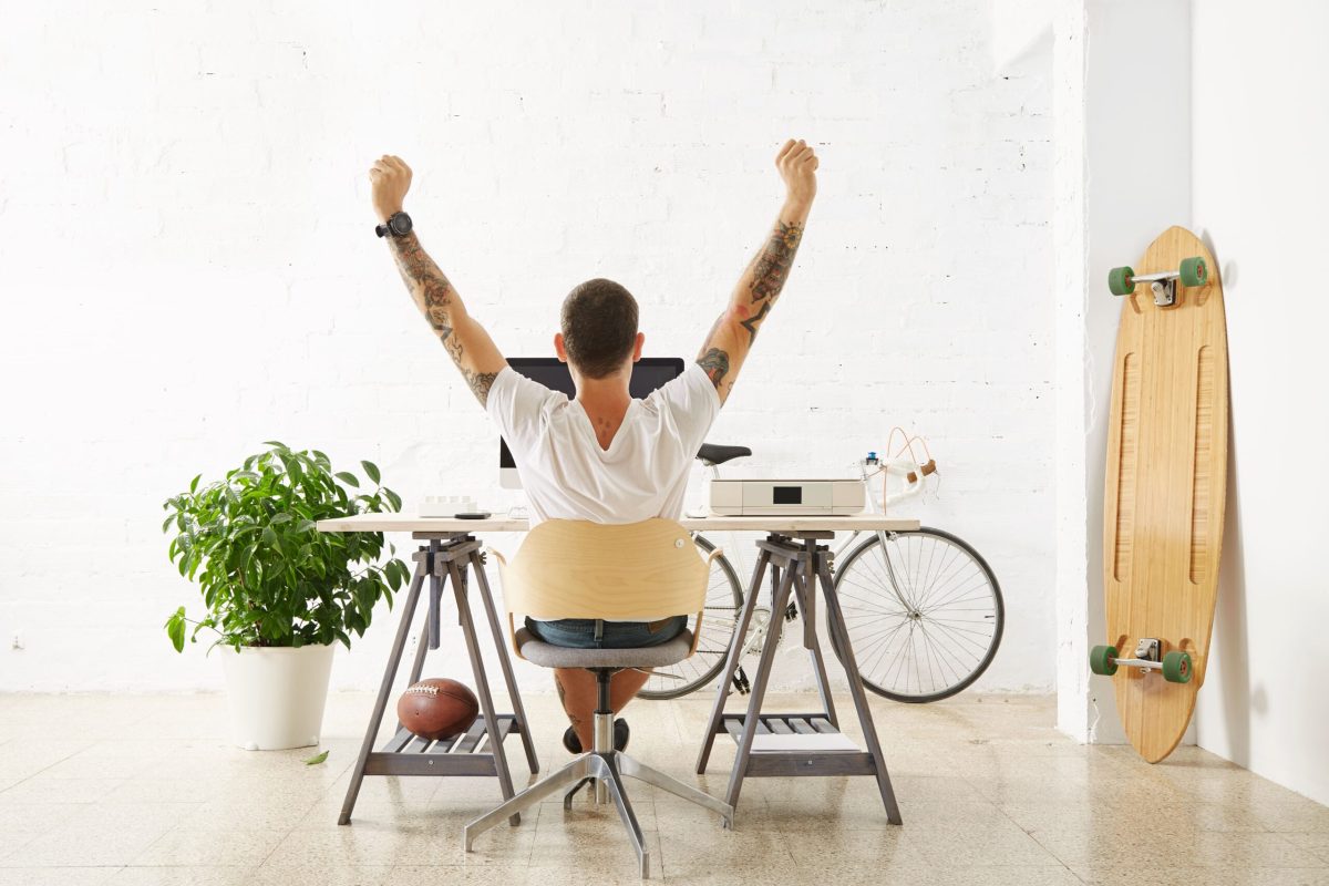 afortunado-freelancer-tatuado-frente-su-espacio-trabajo-rodeado-sus-juguetes-hobby-longboard-bicicleta-vintage-planta-verde-estirando-su-mano-aire-mientras-hace-descanso (1)